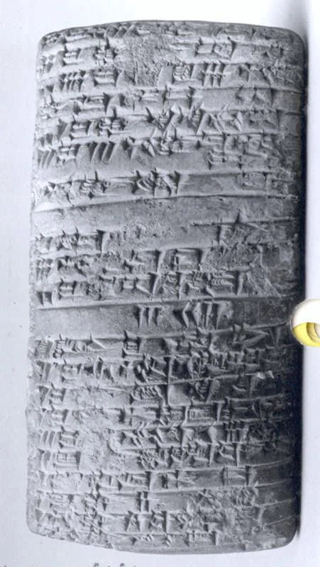 İki yüzü de yatay sıralar hâlinde kama biçimli çivi yazısı işaretleriyle kaplı küçük dikdörtgen kil tablet; sağ kenarda modern ölçek bulunuyor.