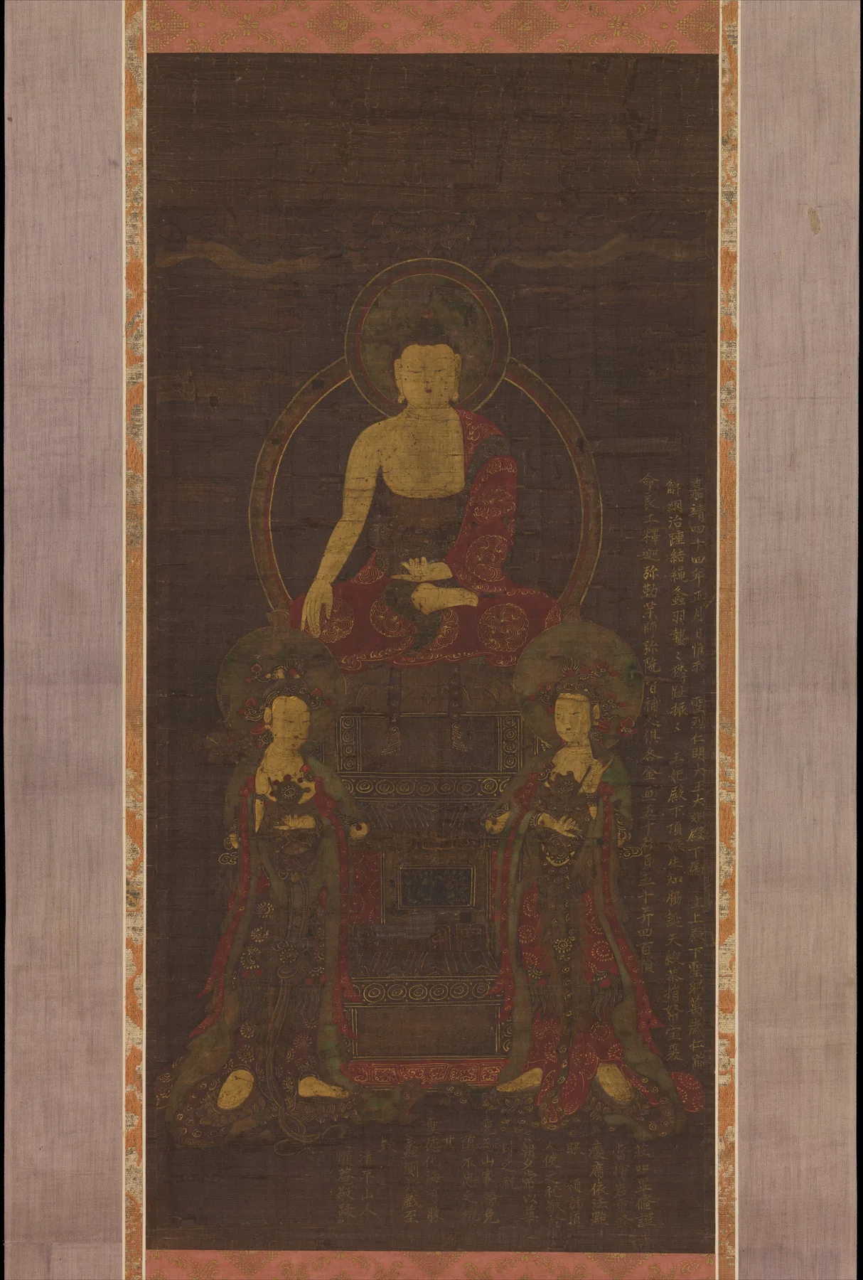Koyu ipek bir Budist asma tomarında Şakyamuni, altın haleler, yazıtlar ve desenli giysiler içinde duran iki bodhisattva arasında bezemeli bir tahtta oturur.