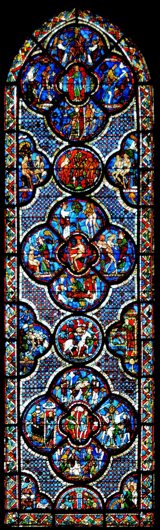 Çok yüksek vitray pencere, koyu mavi, kırmızı, yeşil, altın ve beyaz camdaki küçük kutsal sahneleri içeren birleşik daire ve dört yapraklı bölümlere ayrılmış.