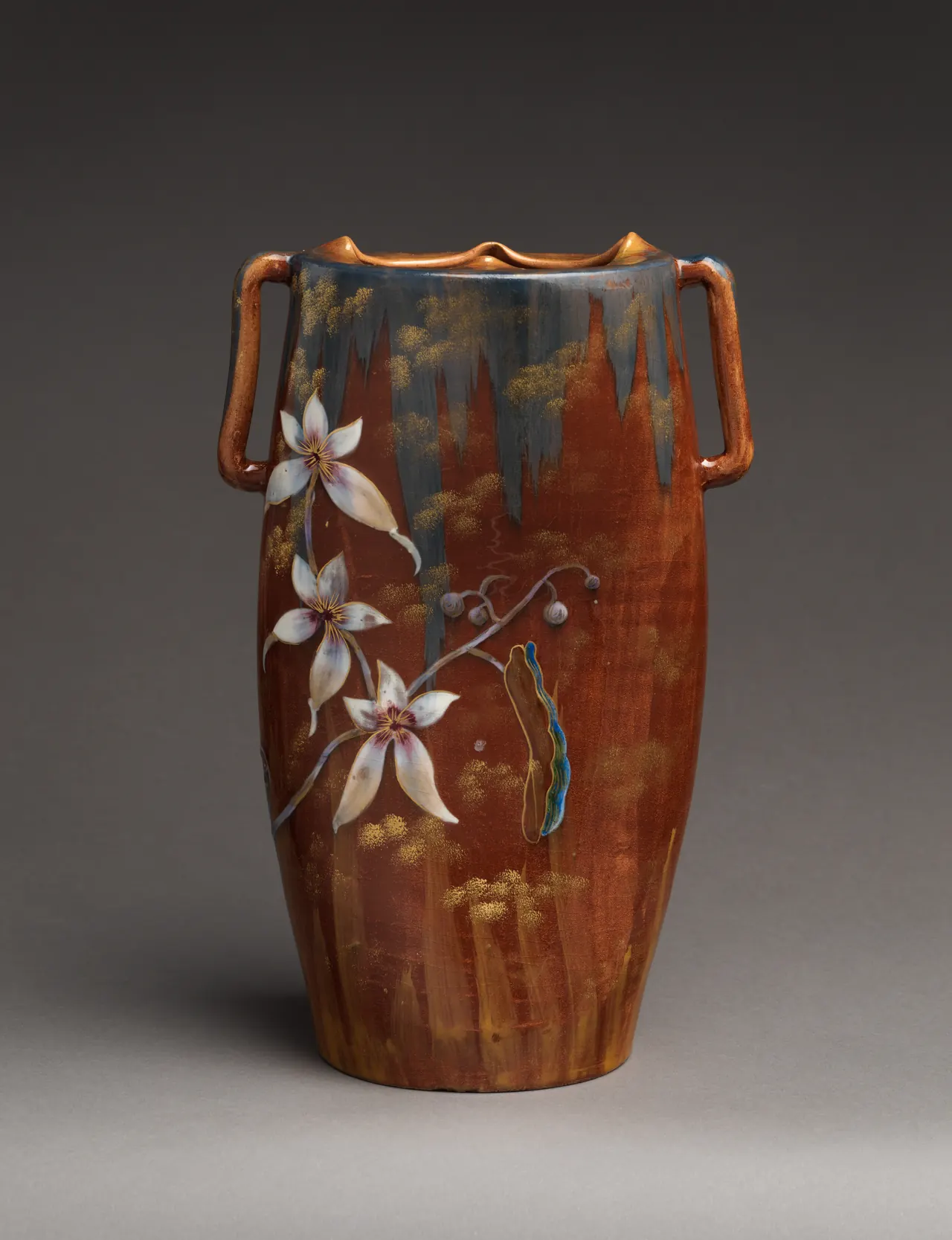 White flowers cross the brown body and dark dripping glaze of Gallé’s tall two-handled ceramic vase