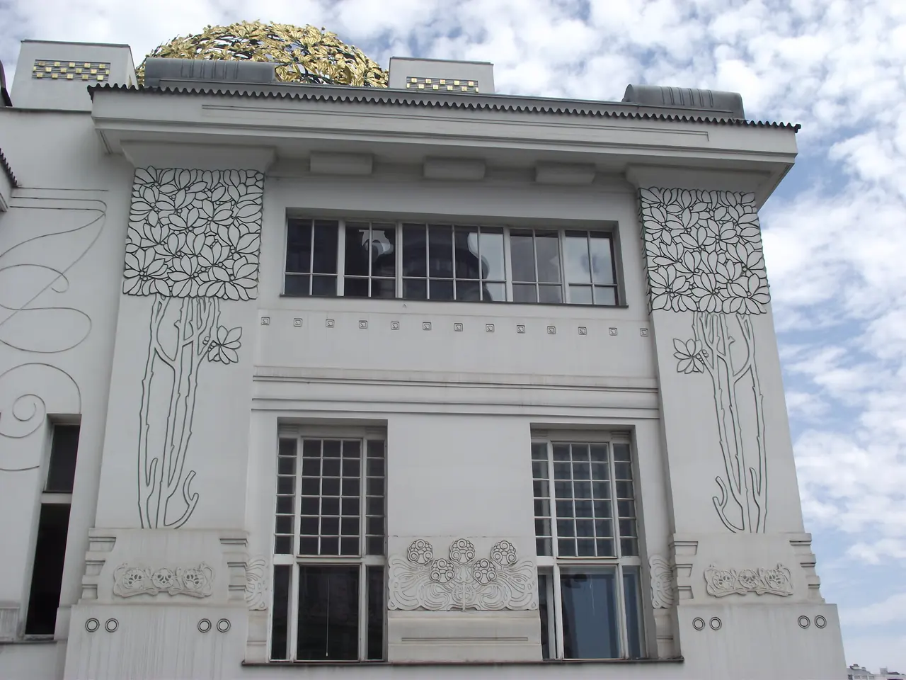 Olbrich’s white Secession building places outlined plants beside rectangular windows beneath part of a gilded dome