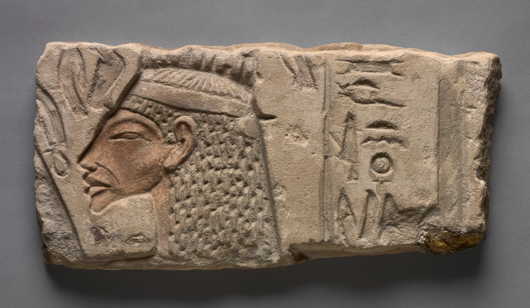 Profilden Nefertiti, elde biten güneş ışını, burnuna uzanan ankh ve hiyeroglif sütunu taşıyan dikdörtgen kumtaşı kabartma parçası.