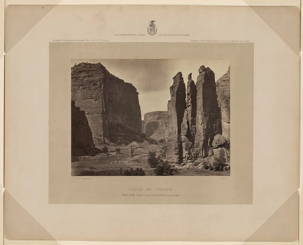 Monte edilmiş albümin fotoğraf, kanyon zeminindeki çok küçük iki insan figürünün üzerinde dev kumtaşı duvarları ve dar kaya kulelerini gösteriyor.