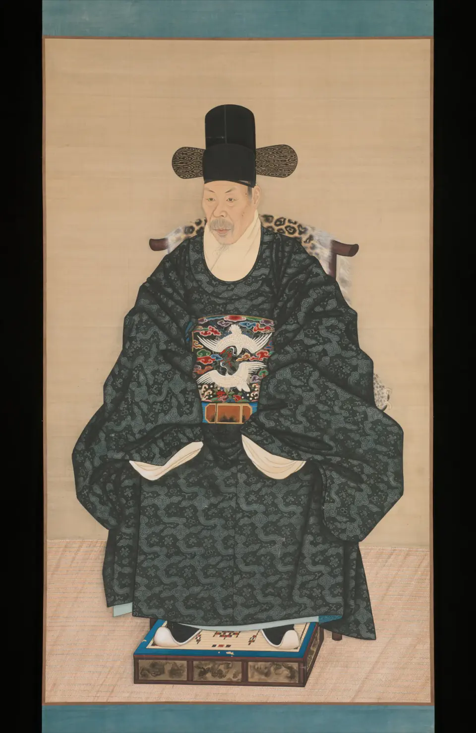 Siyah şapkalı, koyu desenli cüppeli yaşlı bir Joseon bilgin-memuru, boş ipek zemin önünde leopar postu kaplı bir sandalyede cepheden oturur.