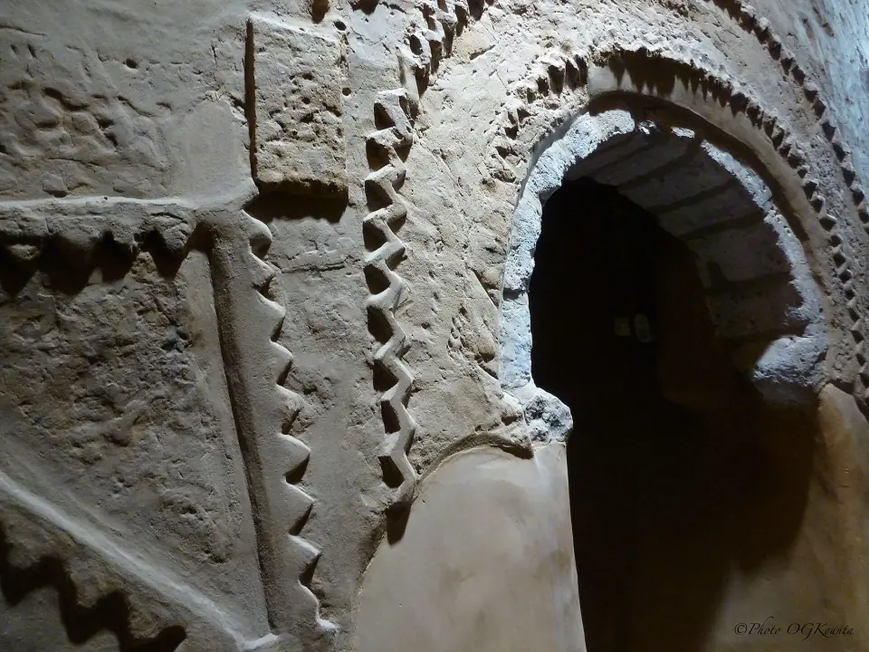 An earthen wall inside Djingareyber Mosque, articulated by projecting triangular forms and a dark arched doorway, shows the grain of plaster and later repair.